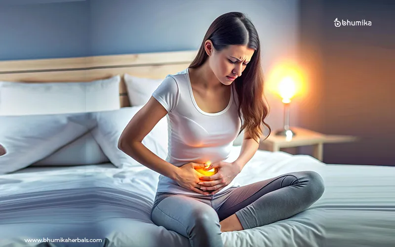 Woman sitting on a bed holding her stomach in discomfort, indicating indigestion.